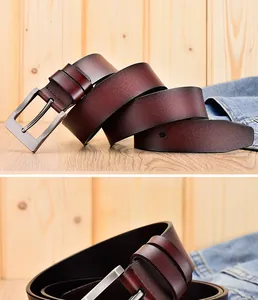 Detail van een donkerbruine echt lederen riem met een matte metalen gesp op houten decor
