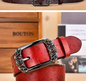 Détail macro d'une boucle en métal vintage et motifs papillons embossés sur ceinture en cuir rouge