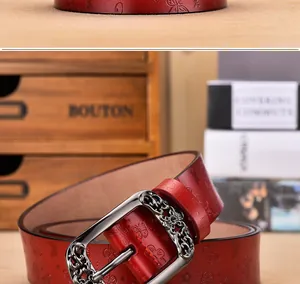 Détail d'une ceinture en cuir rouge avec gaufrage papillon et boucle argentée ciselée