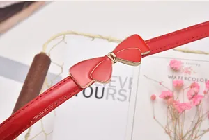 Macro detail of red butterfly buckle on a slim patent leather belt with gold metal accents