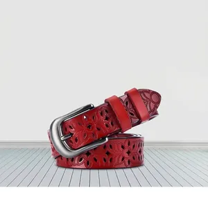 Detail of red leather belt for women featuring intricate floral cutouts and silver pin buckle