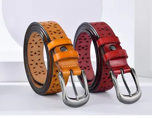 Close-up of orange and burgundy leather belts with hollow floral patterns and metal buckles