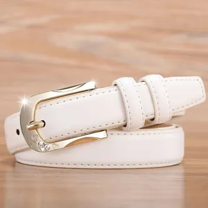 White leather belt with gold heart-shaped rhinestone buckle on a wooden background