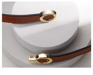 Close-up of brown slim leather belt with gold oval metal buckle on white stone base