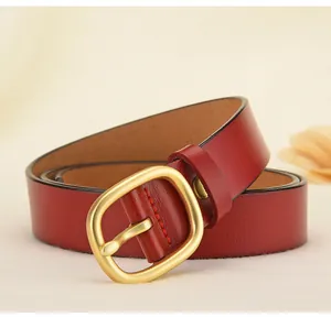 Détail de la ceinture en cuir rouge avec boucle dorée mate et texture de couture