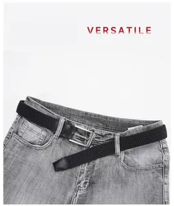 Detalle de cinturón trenzado negro elástico con hebilla plateada en jeans grises
