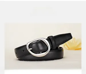Close-up of black leather belt with a polished silver-tone oval buckle on beige surface