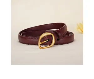Detail of burgundy leather belt with irregular matte gold ring buckle on beige fabric