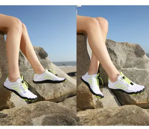 Close-up of lightweight water shoes with white mesh and green laces on beach rocks