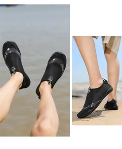 Makroaufnahme atmungsaktiver schwarzer Badeschuhe mit SPORT-Logo am Sandstrand