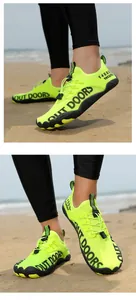 Detail von neongrünen Badeschuhen mit Out-Doors-Schriftzug an einem Sandstrand