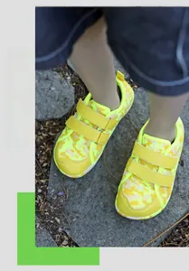Close-up of yellow camouflage barefoot shoes with Velcro straps on outdoor gravel ground