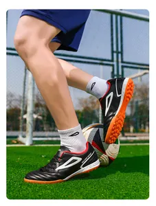 Detalle de botas de fútbol de cuero sintético negro con tacos naranjas en césped artificial