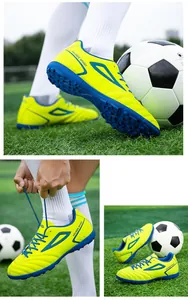 Close-up of fluorescent yellow turf soccer shoes with blue studs on artificial grass