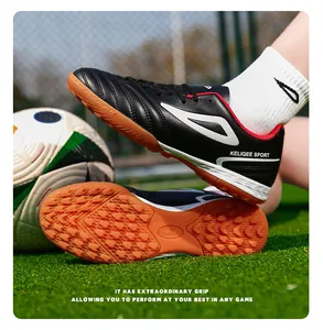 Detalle de zapatillas de fútbol KELIQEE negras con suelas naranjas para césped artificial