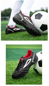 Macro detail of black and red turf soccer shoes with TF studs on synthetic grass