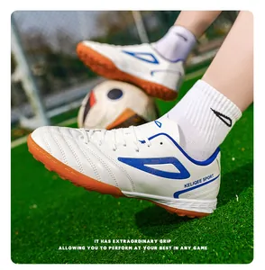 Detalle de botas de fútbol TF blancas con suelas de tacos naranjas en césped real