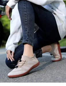 Outdoor view of beige knit fitness shoes with black bungee laces and red rubber soles