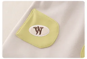 Nahaufnahme der Baby-Strickbekleidung mit gelber Tasche und braunem Buchstabe-W-Stickerei