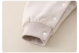 Detailaufnahme von beigem Baumwollstrick mit Rippbündchen und weißen Kunststoff-Druckknöpfen
