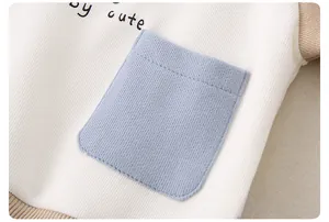 Detail aus weichem Rippbaumwollstoff mit by cute Stickerei und blauer aufgesetzter Tasche