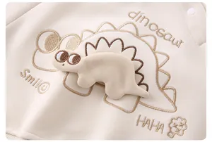 Dettaglio del ricamo dinosauro 3D e del cotone sulla felpa beige per neonati