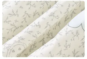 Close-up of soft beige fabric with delicate green leaf print and cartoon heart patterns
