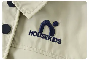 Dettaglio della giacca kaki con bottoni neri e logo HOUSEKIDS ricamato blu