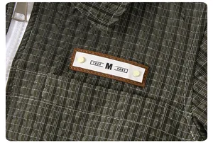 Macro detail of olive green plaid jacket with branded patch and silver metal zipper