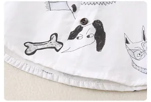 Dettaglio di camicia in cotone bianco con motivi di cani disegnati e bottone in legno