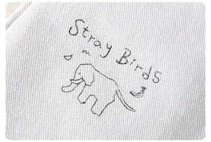 Dettaglio del tessuto in cotone con ricamo di cane carino e testo Stray Birds