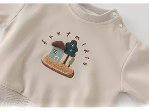 Détail du sweat beige pour bébé avec boutons à l'épaule et broderie artistique fine