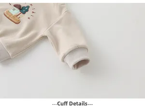 Détail du poignet élastique et broderie de maison sur le sweat beige pour enfant