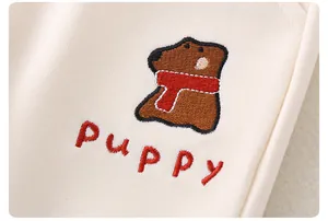 Detailaufnahme von süßer Welpenstickerei und PUKKY-Schriftzug auf beiger Babykleidung