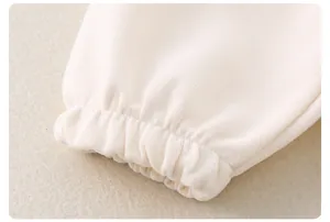 Detailaufnahme der gerippten Bündchen an weichem cremefarbenem Baumwoll-Babystrickset