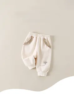 Dettaglio dei pantaloni per neonata color panna con ricamo a fungo e tasche a volant