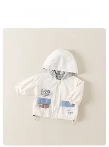Detail of hooded kids jacket with bear embroidery and blue pockets on cream fabric