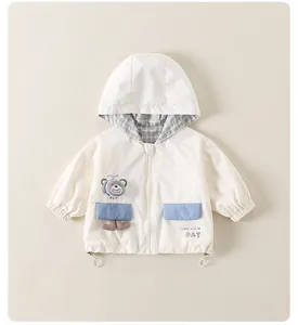 Detail of baby hooded windbreaker with bear patch and blue pockets on beige fabric