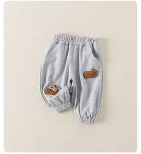 Detail of grey kids joggers featuring elastic waist and cute brown plush bear patch