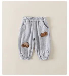 Detail of light gray toddler pants with elastic waistband and dinosaur plush patch