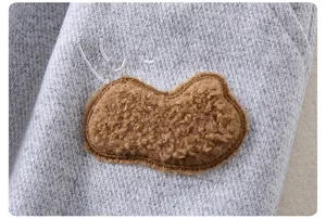 Detail of grey knitted fabric featuring a brown teddy fleece patch with a smiley face