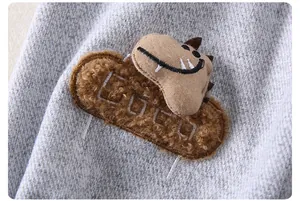 Close-up of a brown dinosaur patch and COCO embroidery on grey knitted boy's trousers