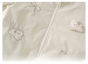 Close-up of cream hooded jacket with floral embroidery, cat pattern, and plush bunny detail