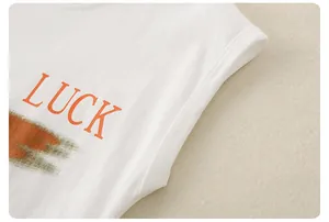 Close-up of boys white cotton T-shirt with orange LUCK print and artistic brushstrokes