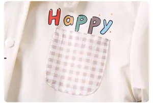 Détail d'une chemise bébé en coton crème avec imprimé Happy et poche à carreaux