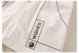 Close-up of white cotton fabric featuring 'WISHES' text print and a brown resin button