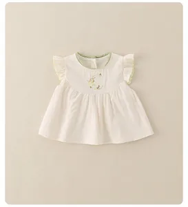 Détail d'un haut bébé fille avec dentelle verte et broderie florale sur tissu crème