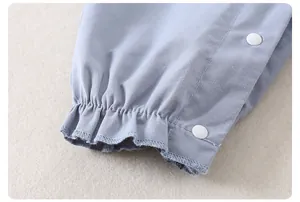 Detail der Baby-Latzhose mit hellblauem Baumwollstoff, Rüschen und weißen Druckknöpfen