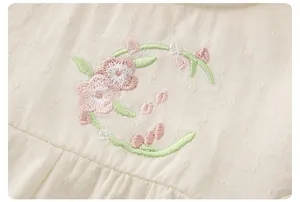 Gros plan détaillé de broderies florales sur vêtement bébé en coton beige doux