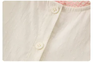 Détail du tissu à losanges crème avec col en dentelle rose et boutons blancs